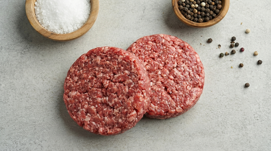 Aged Steak Burgers: two raw burger patties beside bowls of salt and peppercorns