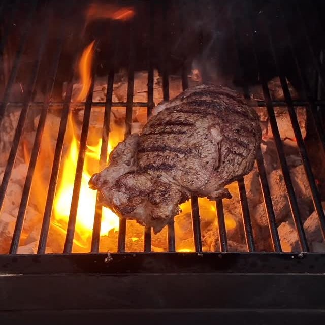 An aged ribeye steak cooking on a charcoal grill