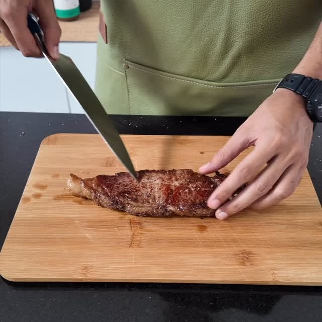 A cooked sirloin steak being sliced on a wooden board